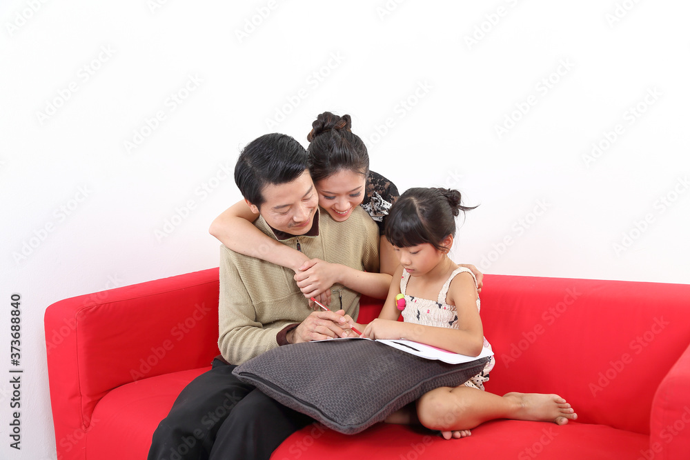South East Asian young couple father mother daughter parent girl child on red sofa read write study book on white background South East Asian young couple father mother daughter parent girl child on red sofa read write study book on white background