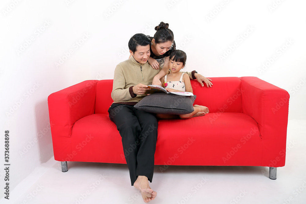 South East Asian young couple father mother daughter parent girl child on red sofa read write study book on white background