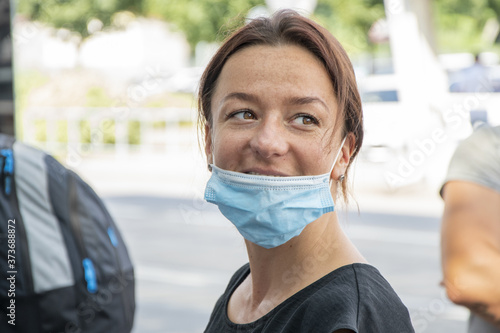 Street portrait of a laughing woman in a medical mask, close-up, selective focus.