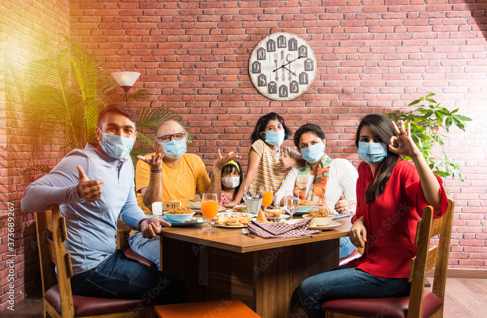 Indian family wears face mask while eating food in restaurant after corona pandemic unlock - concept showing new normal lifestyle in India - obrazy, fototapety, plakaty 