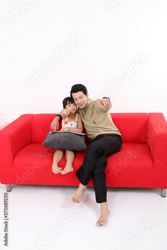 South East Asian young father daughter girl child on red sofa study read book on white background point at camera