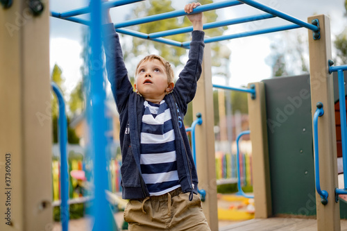 Canvas Print a boy hanging on monkey bar, his brother peep out anove his head