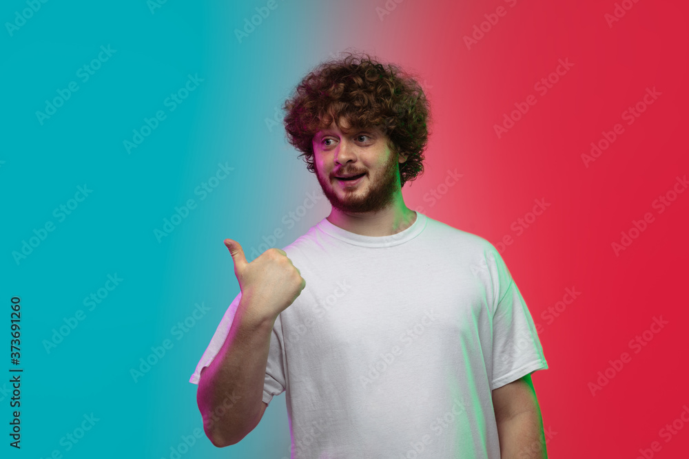 Pointing, showing. Caucasian young man's portrait on gradient studio background in neon light. Beautiful male model in casual style. Concept of human emotions, facial expression, youth, sales, ad. Pointing, showing. Caucasian young man's portrait on gradient studio background in neon light. Beautiful male model in casual style. Concept of human emotions, facial expression, youth, sales, ad.