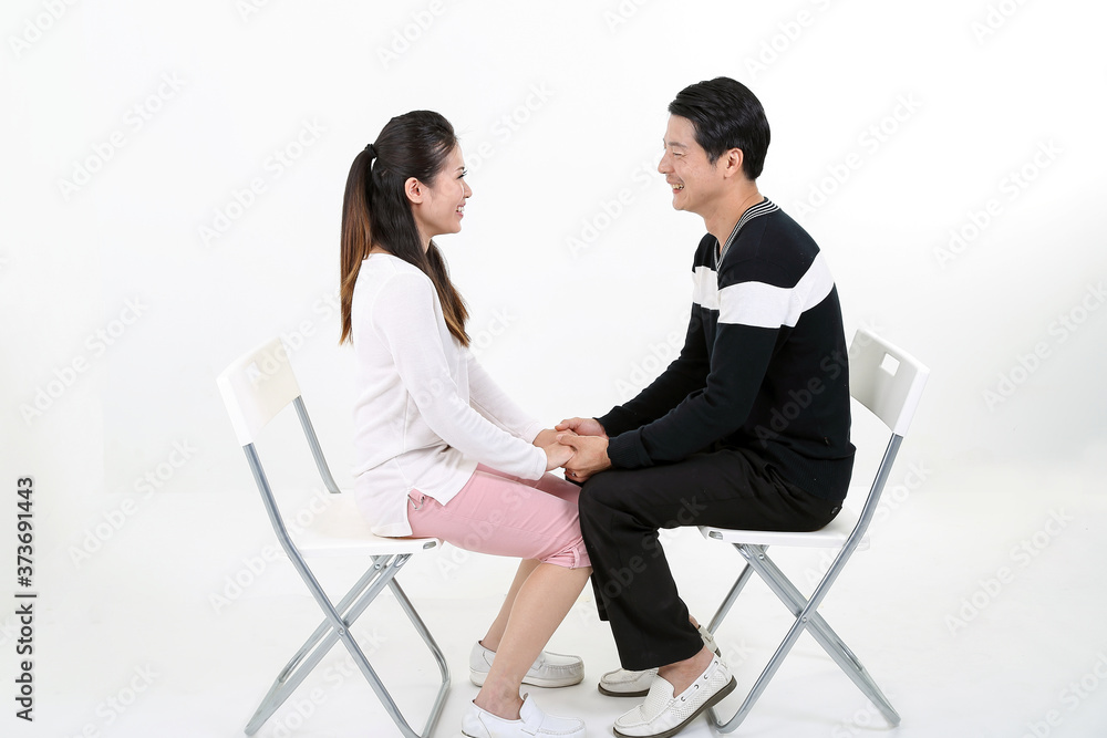Obraz premium South East Asian young Chinese couple husband wife happy love sit on white chair white background face to face holding hand