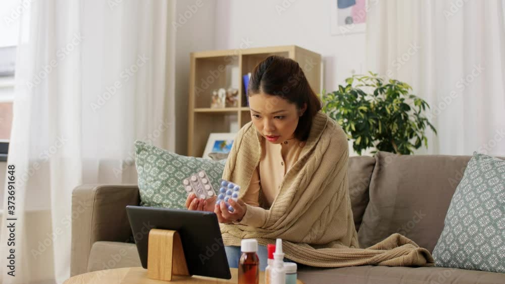 healthcare, technology and people concept - sick asian woman in blanket with medicine having video call on tablet pc computer at home healthcare, technology and people concept - sick asian woman in blanket with medicine having video call on tablet pc computer at home