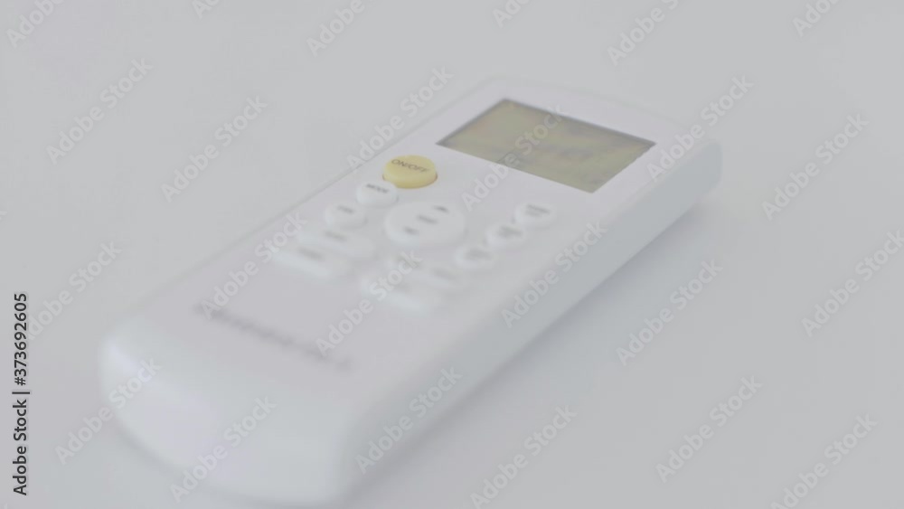 A hand is placing an air conditioning controller in a white table. The controller has a small screen and orange button. A hand is placing an air conditioning controller in a white table. The controller has a small screen and orange button.