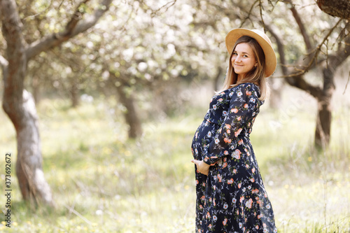 pregnant woman among the flowers. enjoys the beauty of spring among the flowering trees.Reuniting with nature in a flowering spring garden.