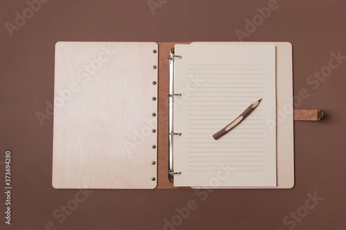 Opened big wooden notebook with pen ready to write on brown colored paper background. Top view