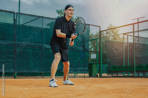 Distant plan of Man Holding Racket In Both Hands To Straighten Strike While Waiting For Ball Serving At Tennis Court © Akaberka