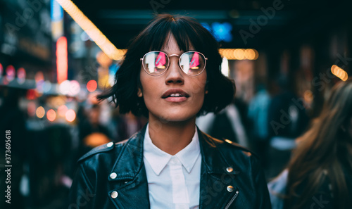 Caucasian woman in optical spectacles with neon reflection of lights standing at urbanity during travel vacations for visiting New York, attractive hipster girl in trendy apparel going out #373695618