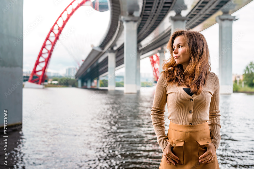 A young woman with long hair stands under a bridge overlooking the picturesque red bridge in Moscow