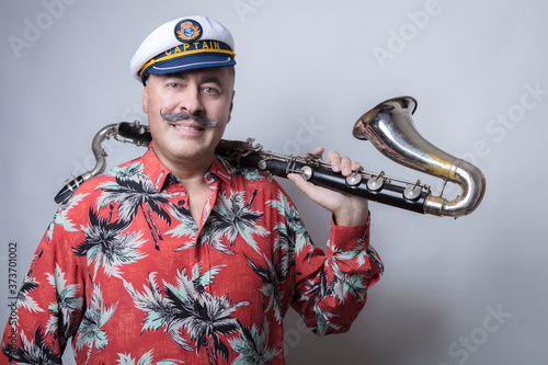 A man smiles and looks at the camera with a beautiful, long mustache in a marine captain's cap, holds a bass clarinet on his arm, photo in the studio light background, close-up photo