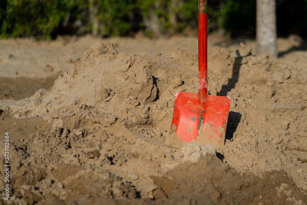 A red shovel (working equipment of construction industrial) is stabbing on the sand bulk. A red shovel (working equipment of construction industrial) is stabbing on the sand bulk.