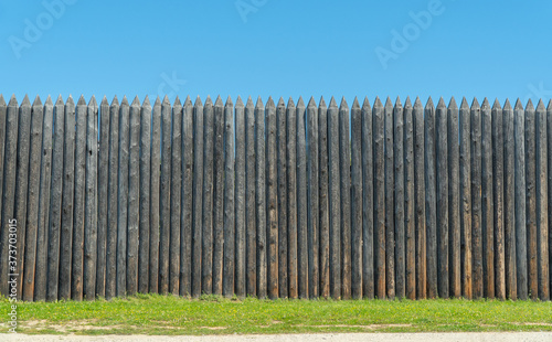 The fence is made of uncouth logs. palisade are rough and pointed to the top