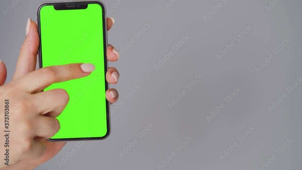 Female hands using a smartphone with a green screen on a gray background. Chroma key. Female hands using a smartphone with a green screen on a gray background. Chroma key.