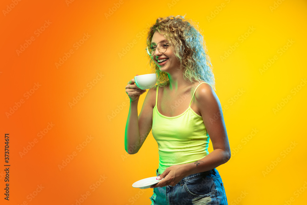 Coffee time. Caucasian young woman's portrait isolated on gradient studio background in neon. Beautiful female curly model in casual style. Concept of human emotions, facial expression, youth, sales Coffee time. Caucasian young woman's portrait isolated on gradient studio background in neon. Beautiful female curly model in casual style. Concept of human emotions, facial expression, youth, sales