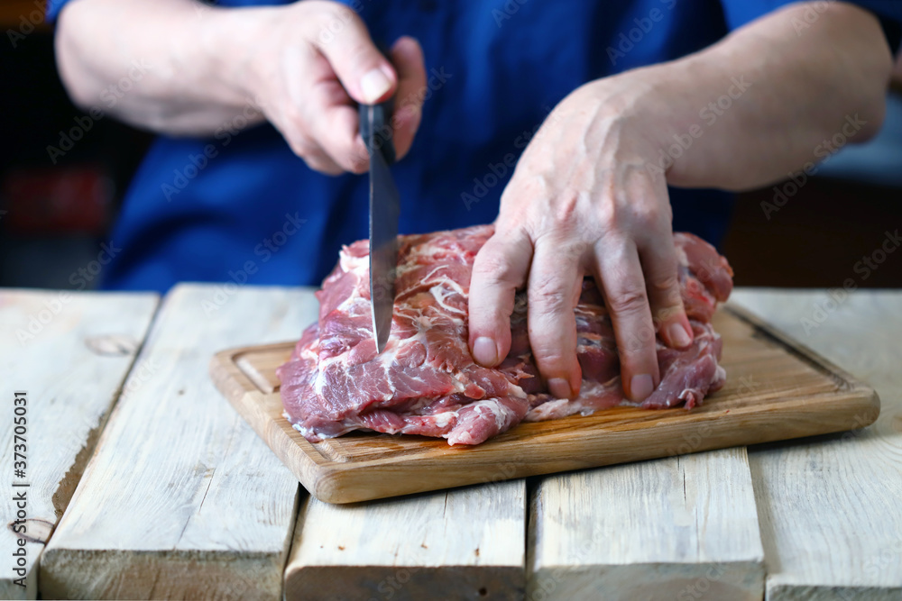 Selective focus. Macro. Raw pork meat in the hands of a chef with a knife. A chef with a knife cuts a raw pork neck. Raw pork on a cutting board.