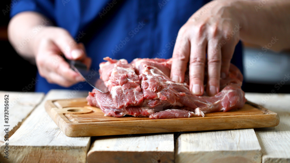 Selective focus. Macro. Raw pork meat in the hands of a chef with a knife. A chef with a knife cuts a raw pork neck. Raw pork on a cutting board.