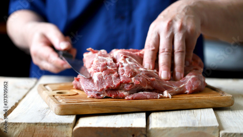 Fototapeta Naklejka Na Ścianę i Meble -  Selective focus. Macro. Raw pork meat in the hands of a chef with a knife. A chef with a knife cuts a raw pork neck. Raw pork on a cutting board.