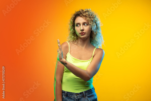 Greeting. Caucasian young woman s portrait isolated on gradient studio background in neon. Beautiful female curly model in casual style. Concept of human emotions  facial expression  youth  sales  ad.
