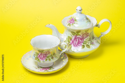 Tea set on a yellow background. A cup and saucer and a teapot next to it. Tea set with flower decorations