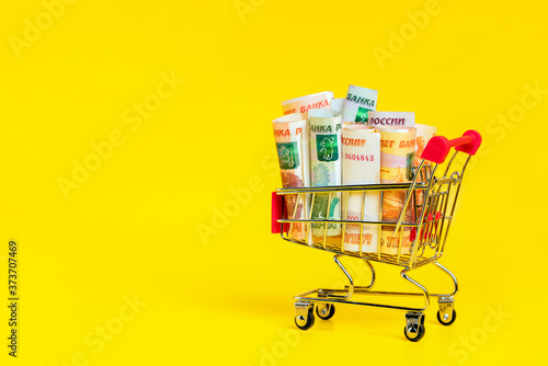 Russian ruble banknotes in shopping cart on yellow background. Copy space for text