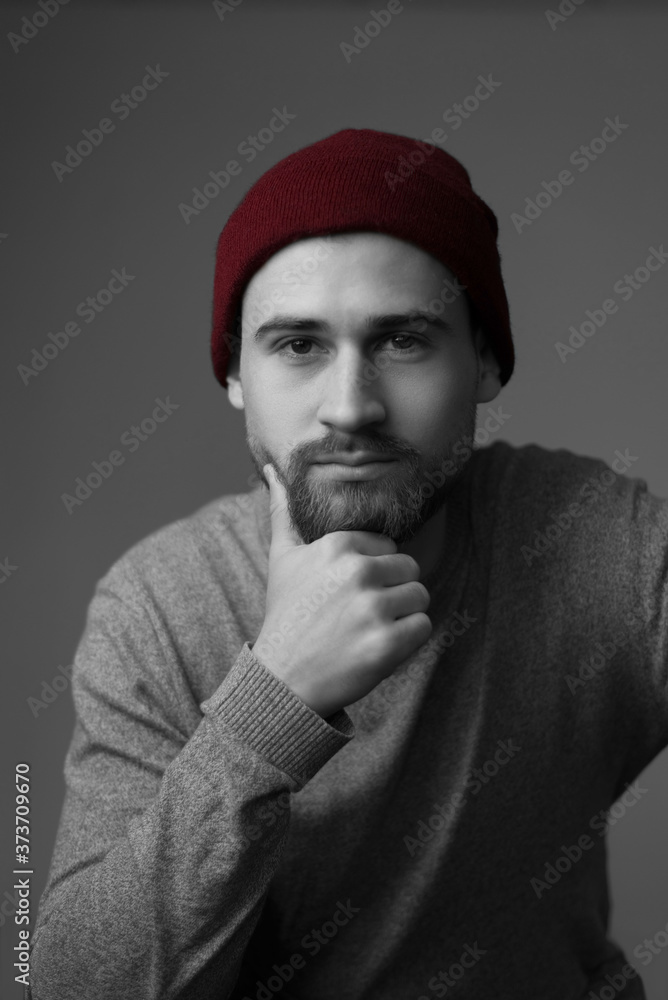 Portrait of a young bearded guy in a sweater, and a red hat, smiling. Studio photo on a gray background. Portrait of a young bearded guy in a sweater, and a red hat, smiling. Studio photo on a gray background.