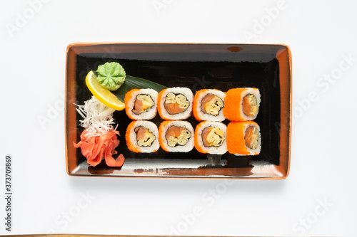 A portion of maki sushi with an assortment of Japanese side dishes in a rectangular ceramic plate on a white plate. Top view.