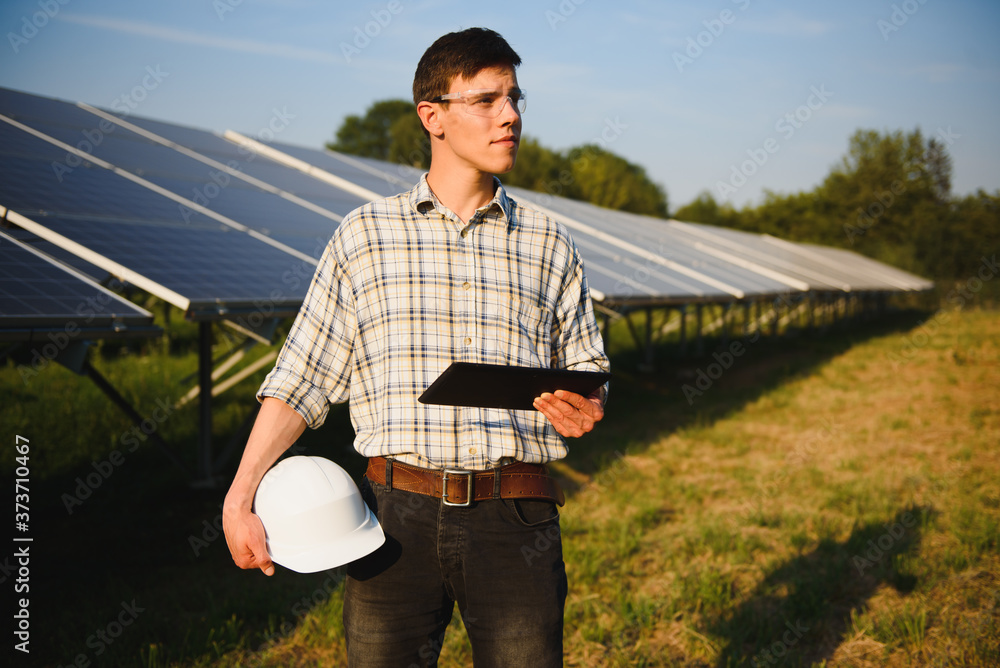 The portrait of a young engineer checks with tablet operation with sun, cleanliness on field of photovoltaic solar panels. Concept: renewable energy, technology, electricity, service, green power. The portrait of a young engineer checks with tablet operation with sun, cleanliness on field of photovoltaic solar panels. Concept: renewable energy, technology, electricity, service, green power.