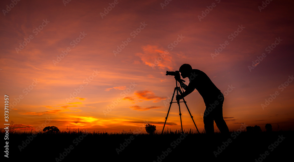 Silhouette of photographer on open field at sunset background.