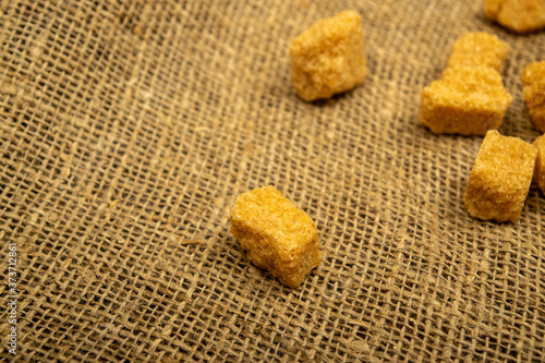 Pieces of brown cane sugar on a background of homespun fabric with a rough texture. Close up.