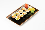 A portion of maki sushi with an assortment of Japanese side dishes in a rectangular ceramic plate on a white plate.