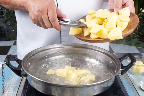 Chef pouring raw potatoes from a wooden Board into boiling water in a pot