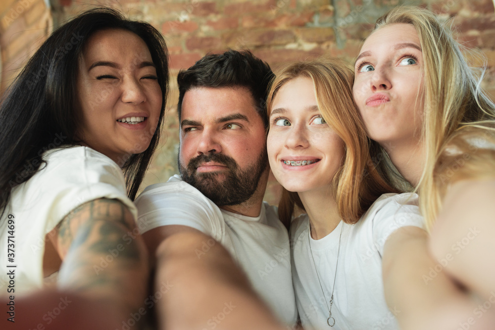 Fototapeta premium Taking selfie together. Group of adorable multiethnic friends having fun at home. Copyspace. Diversity, inclusion, friendship and love concept. Different nationalities united with sincere emotions.