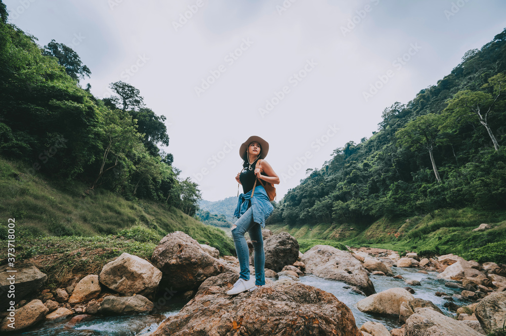 Traveler Asian woman with backpack relaxing and enjoying view of mountain river and forest landscape during vacation. Travel concept