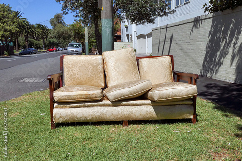 A broken settee is left on the sidewalk in an urban street. The dumping of rubbish is an ongoing problem for the Melbourne municipalities and there is a penalty against leaving garbage on the street. photo