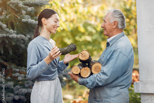 Grandfather with granddaughter. Family on summer yard. Adult man holding firewood. © prostooleh