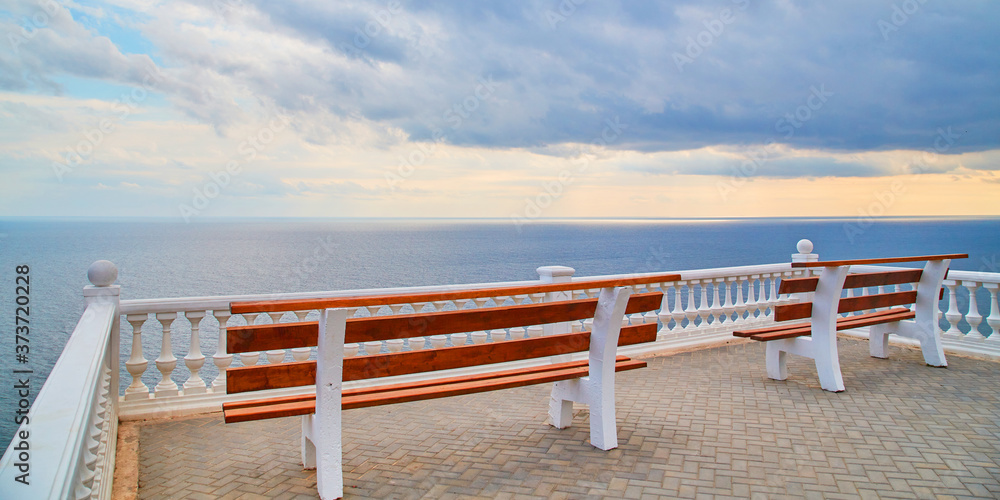 Obraz premium Virgin nature. Summer view. Ocean scenery. Viewing platform with bench. Empty promenade. Stormy dark sky. Calming sea