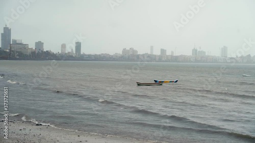 Two Fishing Boats Floating Offshore At The Girgaum Chowpatty Beach In Mumbai, India On A Foggy Day - wide shot photo