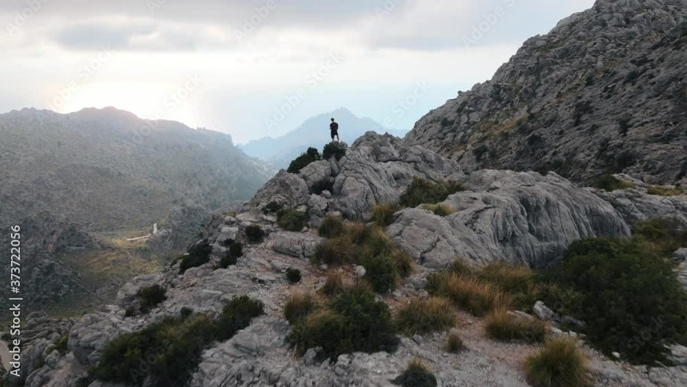 Aerial flying over a man standing at the edge of a cliff and revealing a winding road at sunset Aerial flying over a man standing at the edge of a cliff and revealing a winding road at sunset