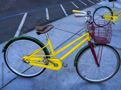 Colorful google bike is parking on the pavement. Bicycle has the colors of google, green yellow and red. Bicycle has a basket to carry.
