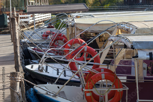 Plenty of small tour boats are tied to the wooden port. Little tour boats are awaiting for the passengers. Rope tied in knot on wooden surface of pier under warm light.