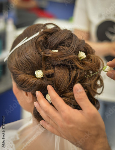 Young woman/bride in wedding dress is getting her hair done before wedding or party. Hairdresser is working on the head of the bride.