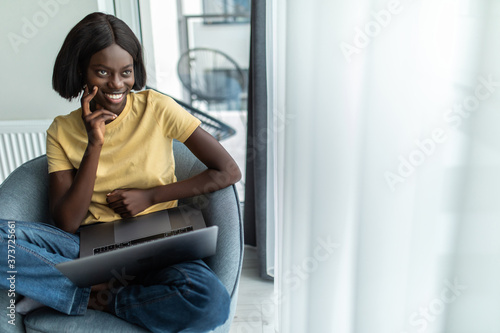 Free Download African american woman using laptop while sitting on chair in living room - GFXLoad