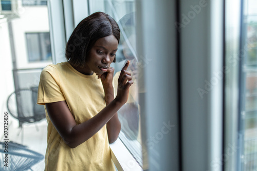 Free Download African american woman standing near windows with placard with stay at home at quarantine lettering in living room - GFXLoad