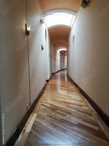 Long corridor with wooden floor with entrance of light and lights on the walls