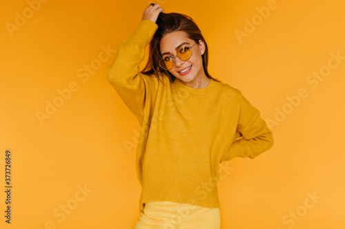 Pleased good-humoured girl in sweater posing with interested smile. Studio shot of glad brunette lady in sunglasses. © Look!