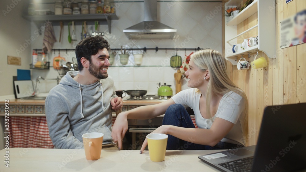 Young happy couple talking during breakfast in the kitchen