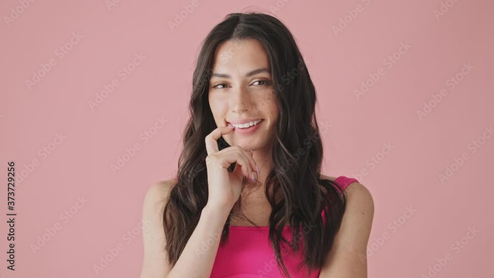 A smiling young woman is thinking about something standing isolated over pink background A smiling young woman is thinking about something standing isolated over pink background