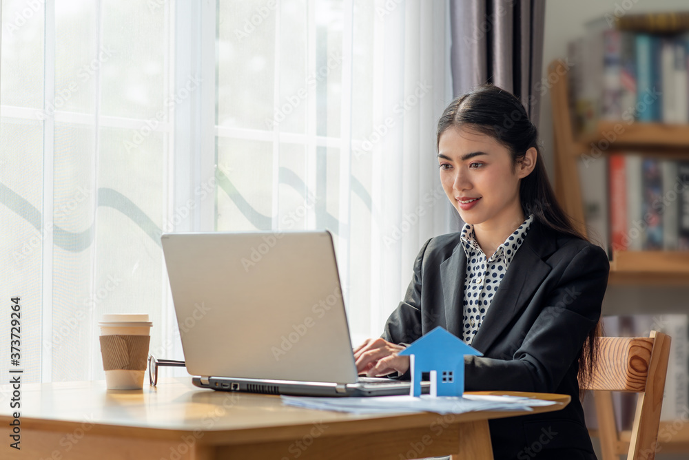 Young Asian business woman working in the office and using her laptop in her office with paper house Young Asian business woman working in the office and using her laptop in her office with paper house